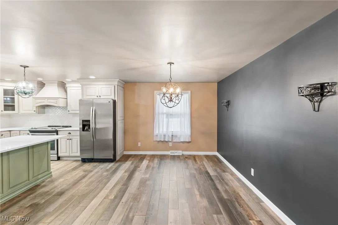 Kitchen with white cabinets, appliances with stainless steel finishes, custom range hood, and an inviting chandelier