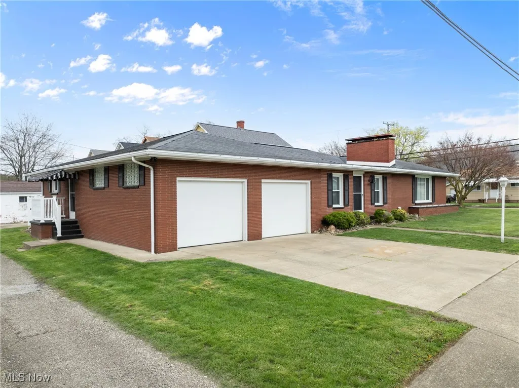 View of front of home with concrete driveway, a chimney, a front yard, brick siding, and a garage