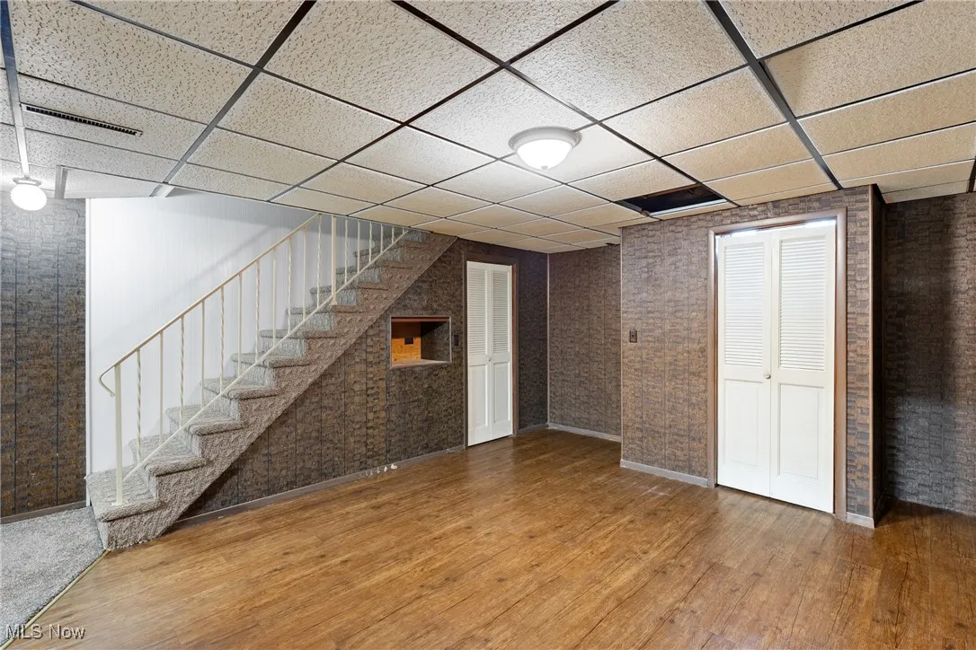 Finished below grade area with brick wall, stairway, a paneled ceiling, and wood finished floors