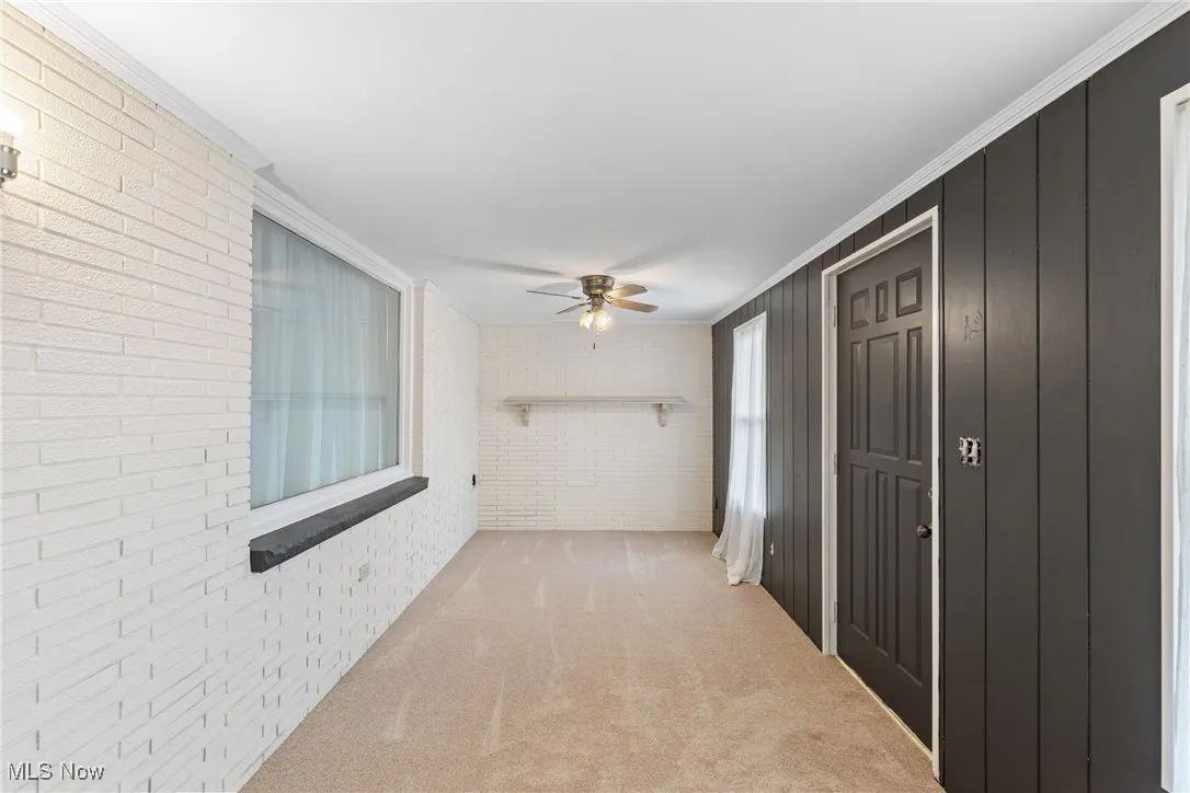 Hallway with brick wall, light colored carpet, and crown molding
