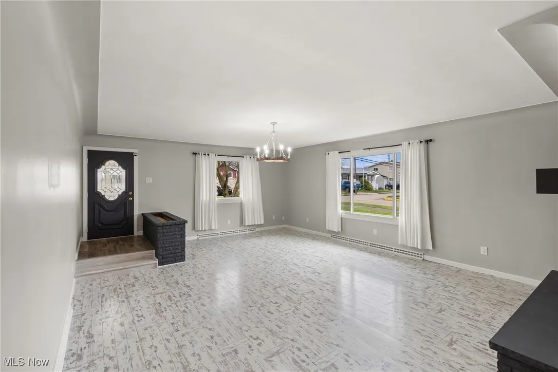 Unfurnished living room with a notable chandelier, a baseboard radiator, baseboards, and wood finished floors