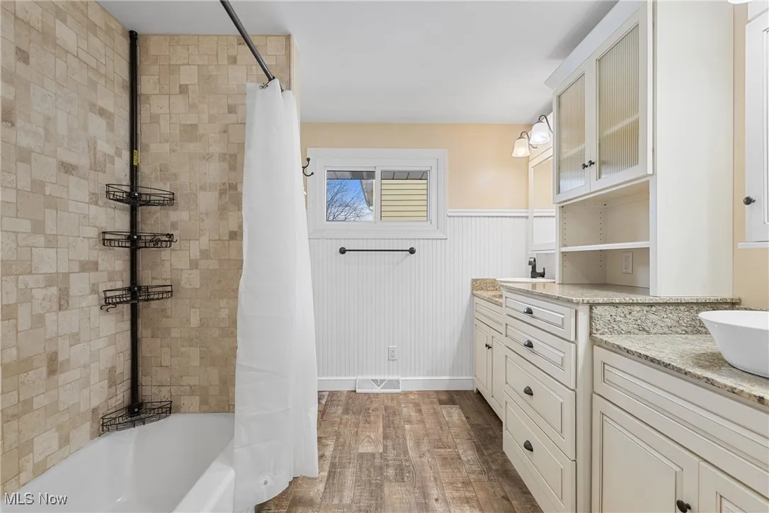 Bathroom with wainscoting, vanity, wood finished floors, and shower / bath combination with curtain