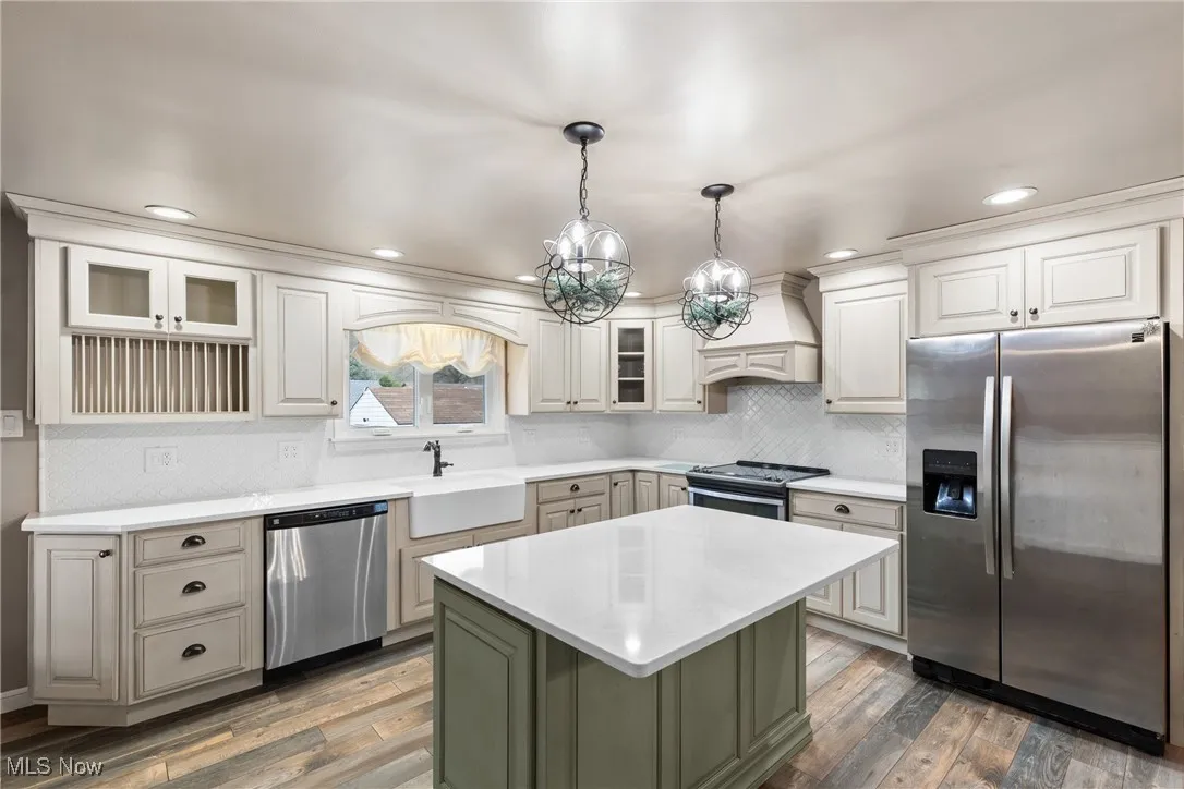 Kitchen with light countertops, premium range hood, stainless steel appliances, hardwood / wood-style flooring, and a sink