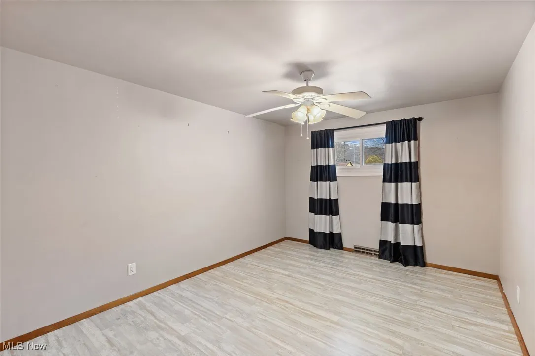 Spare room with baseboards, light wood-type flooring, and ceiling fan
