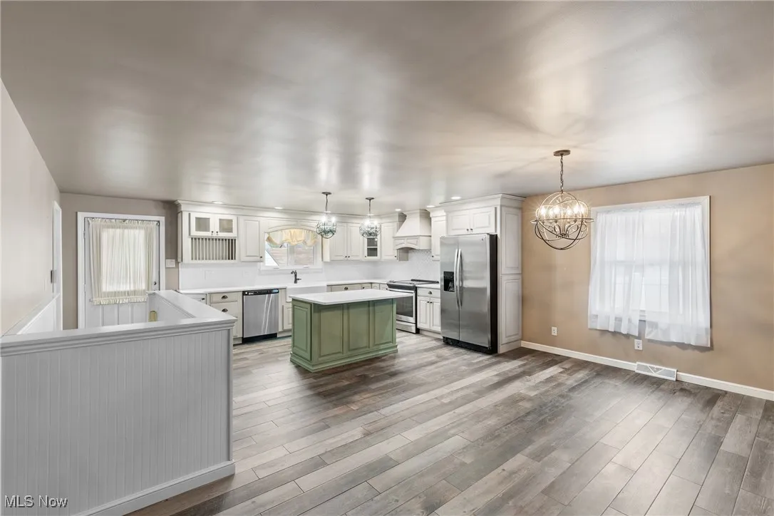 Kitchen with custom range hood, green cabinets, an inviting chandelier, visible vents, and appliances with stainless steel finishes