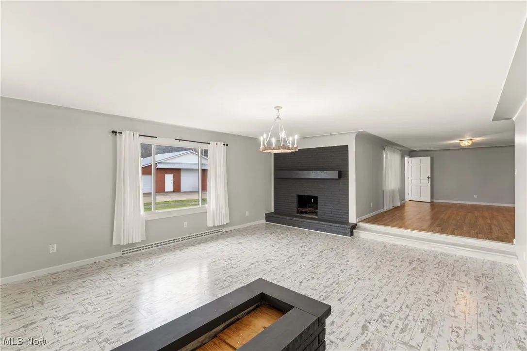 Unfurnished living room featuring wood finished floors, a baseboard heating unit, a notable chandelier, and baseboards