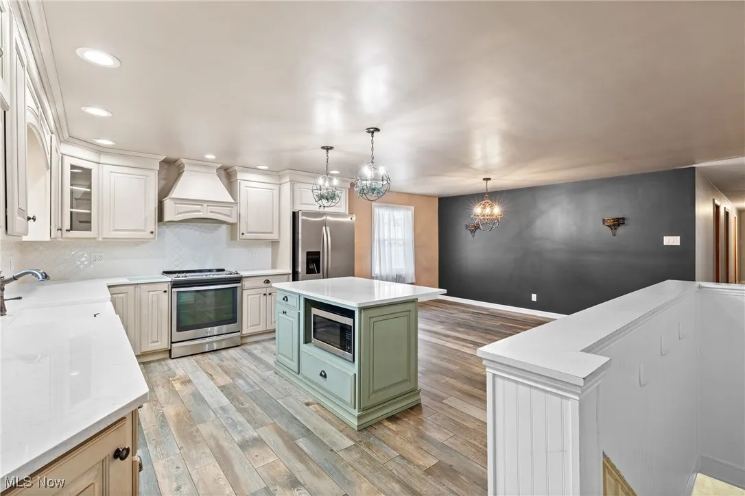 Kitchen with appliances with stainless steel finishes, a sink, premium range hood, light wood finished floors, and a notable chandelier