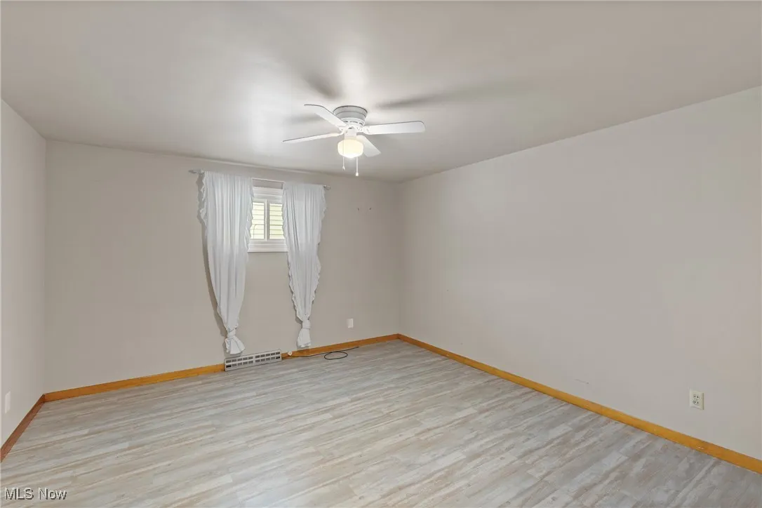 Unfurnished room featuring light wood finished floors, baseboards, a ceiling fan, and visible vents