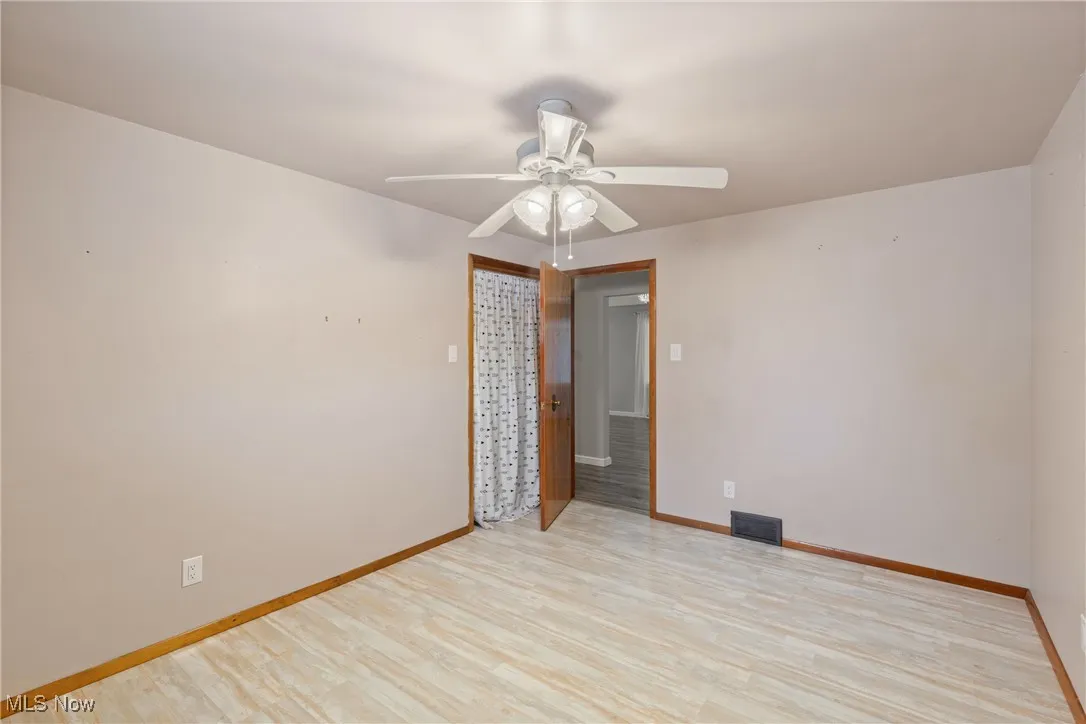 Empty room with light wood finished floors, visible vents, baseboards, and a ceiling fan