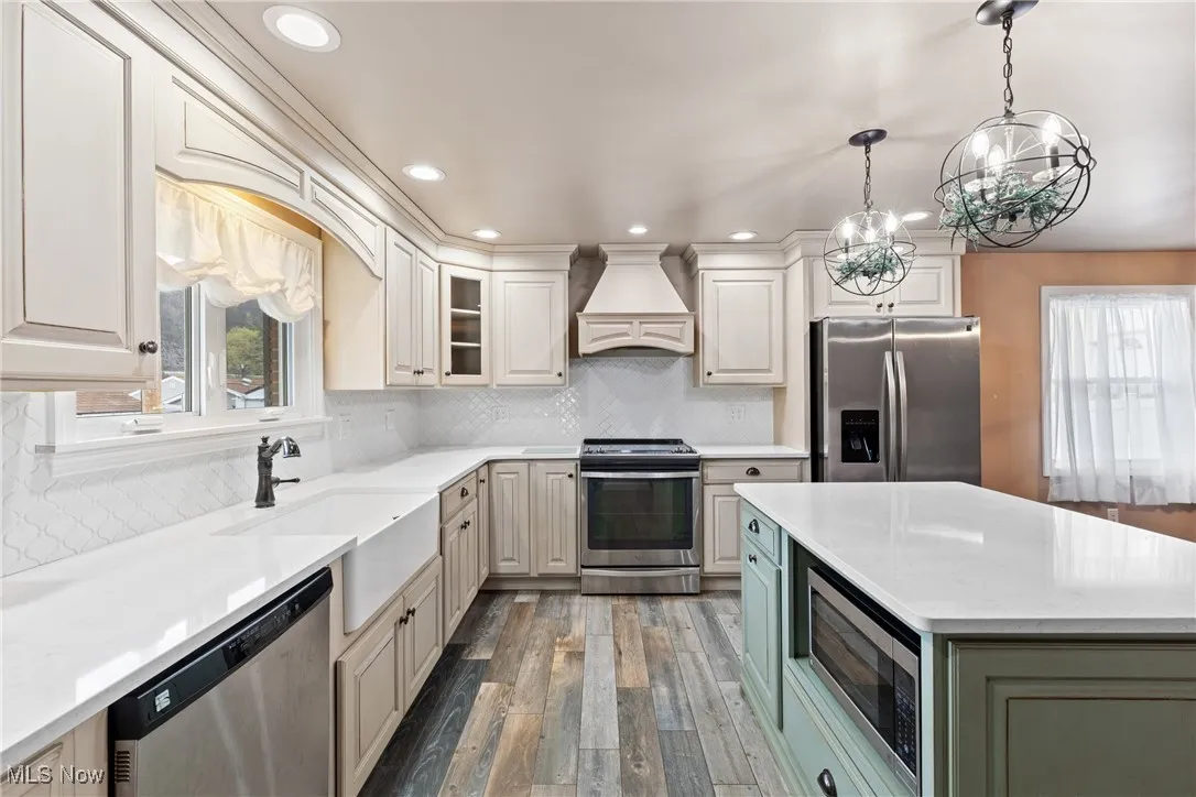 Kitchen with custom exhaust hood, a notable chandelier, appliances with stainless steel finishes, a sink, and wood finished floors