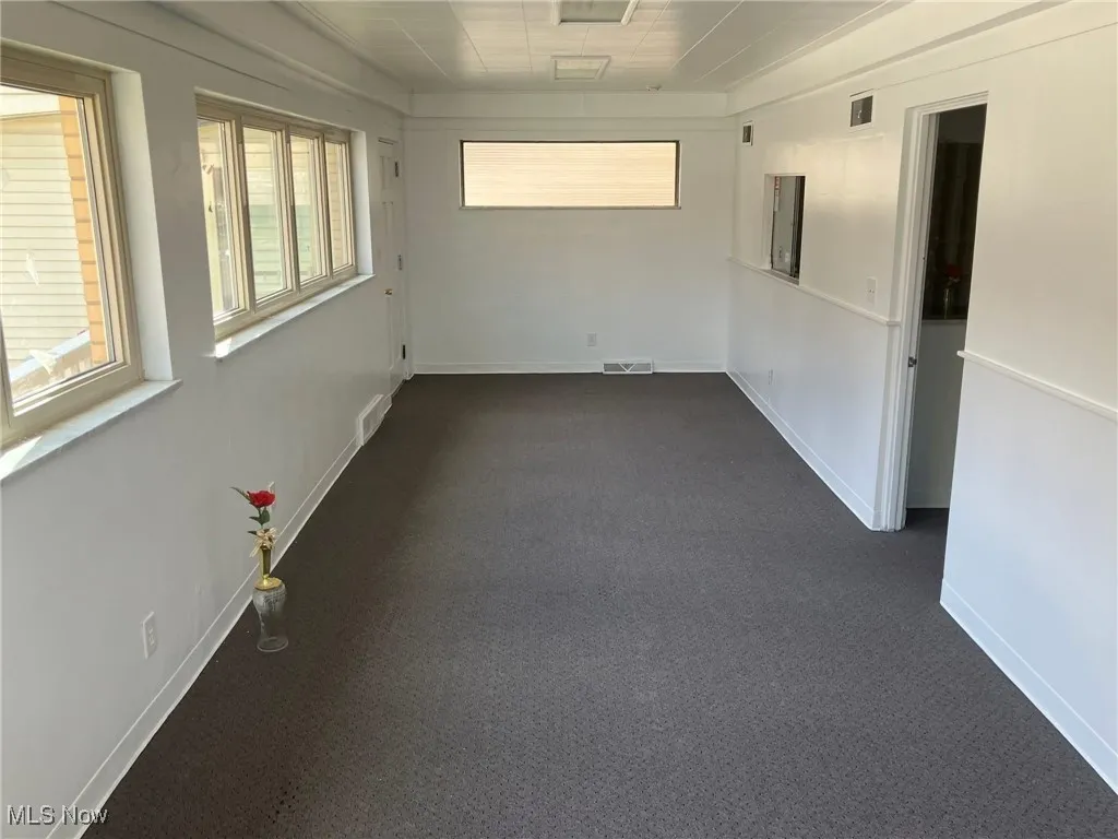 Empty room with dark carpet, baseboards, and visible vents