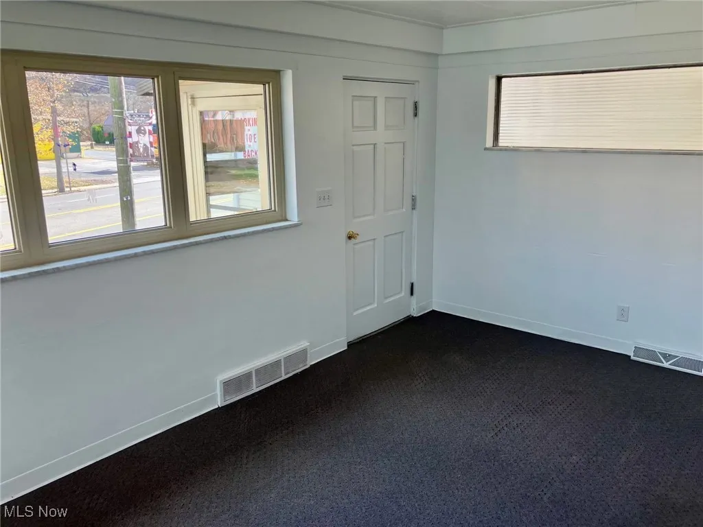 Spare room with baseboards, dark colored carpet, and visible vents