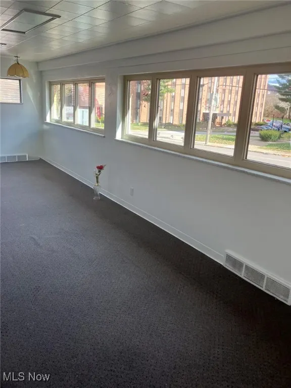 Spare room featuring dark carpet, visible vents, and baseboards