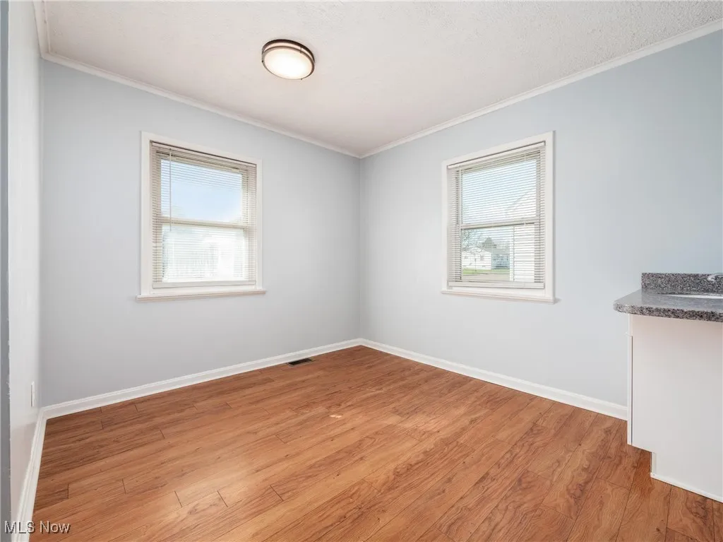 Spare room with plenty of natural light, light wood-style flooring, visible vents, and ornamental molding