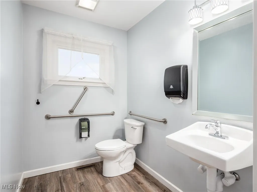 Bathroom featuring visible vents, baseboards, a sink, toilet, and wood finished floors