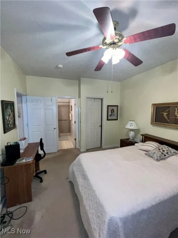 Carpeted bedroom featuring ensuite bath and ceiling fan