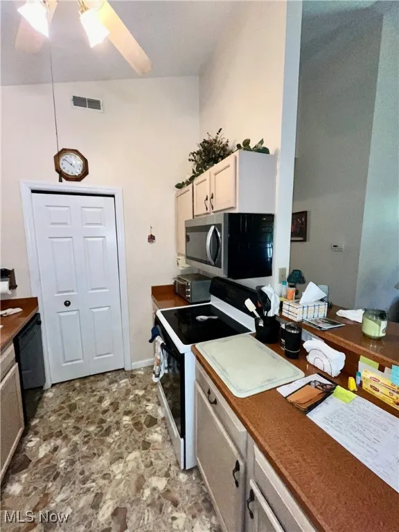 Kitchen featuring stainless steel microwave, a ceiling fan, stone finish floor, visible vents, and electric range oven