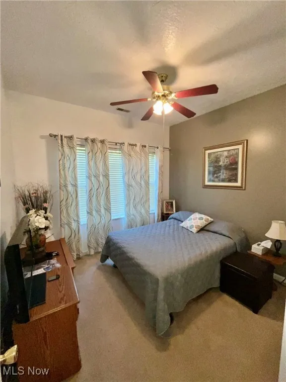 Bedroom with visible vents, a ceiling fan, carpet flooring, and a textured ceiling