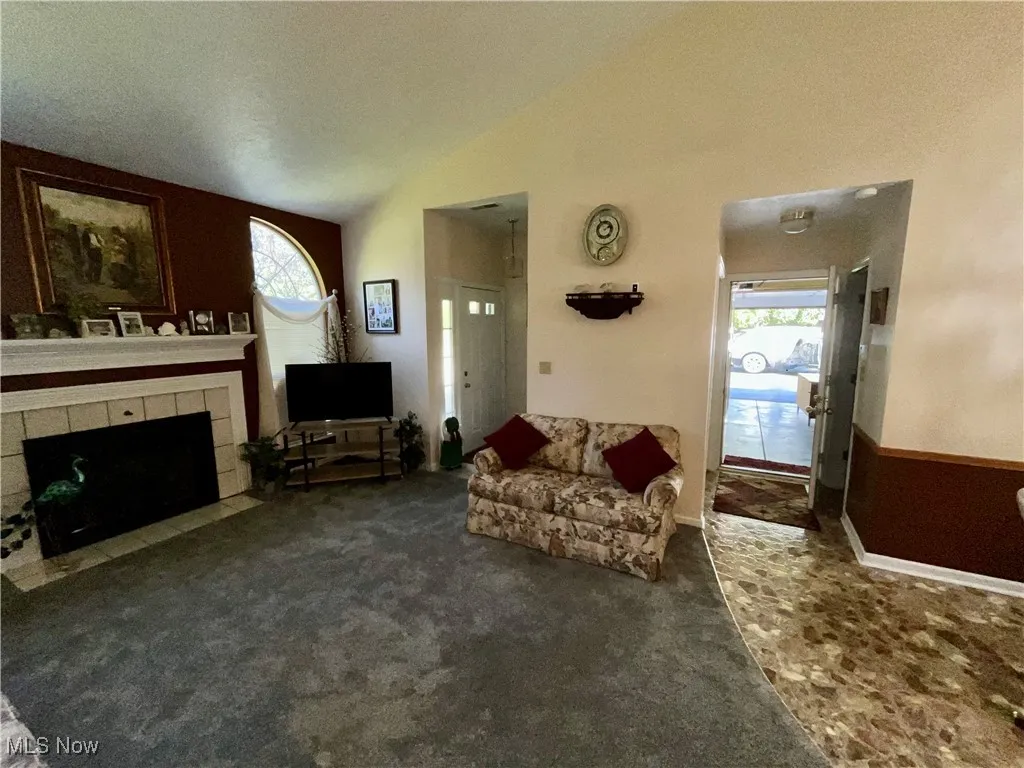 Carpeted living room featuring a wealth of natural light, a tiled fireplace, and vaulted ceiling