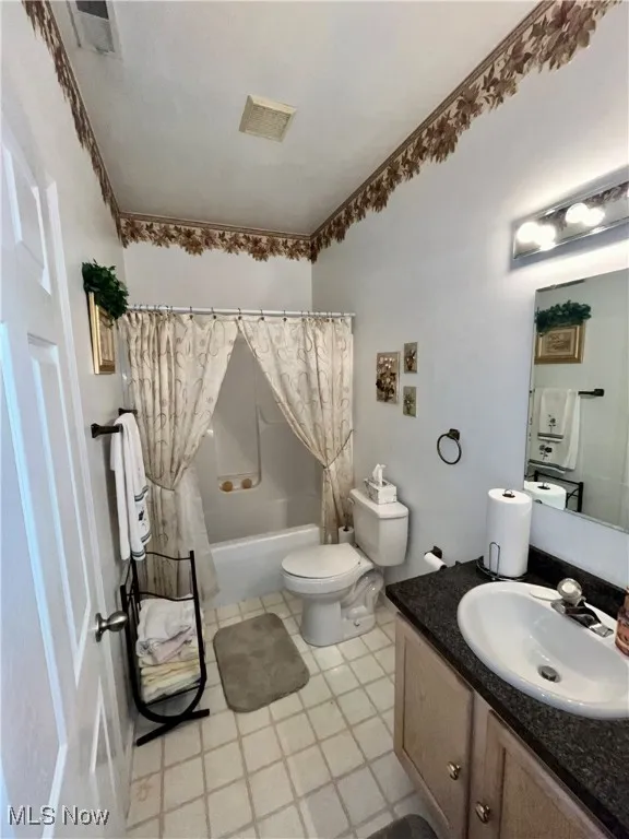 Full bath with visible vents, toilet, shower / bath combo with shower curtain, and vanity