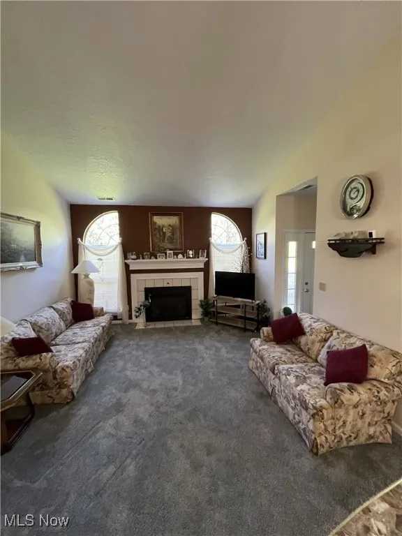 Living area with carpet flooring, a tiled fireplace, and vaulted ceiling