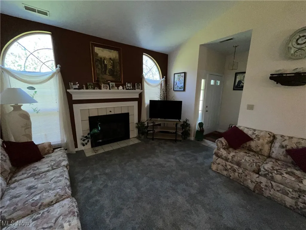 Carpeted living area with a tiled fireplace, visible vents, and vaulted ceiling