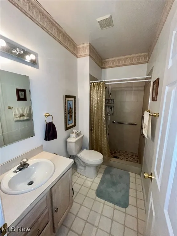 Bathroom with toilet, visible vents, a tile shower, and vanity