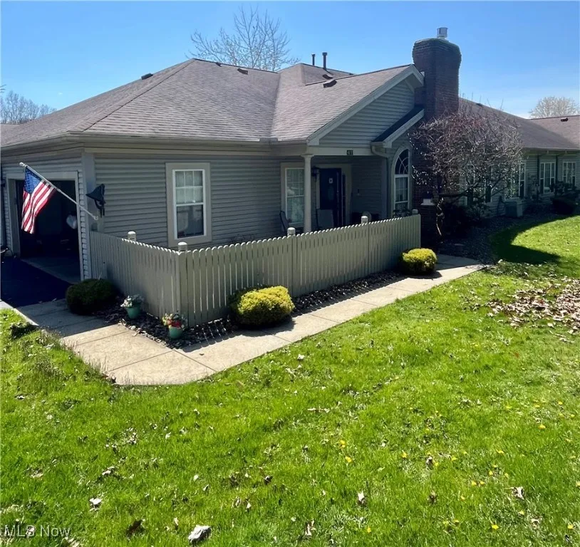Back of house featuring a shingled roof, a chimney, a fenced front yard, and a lawn