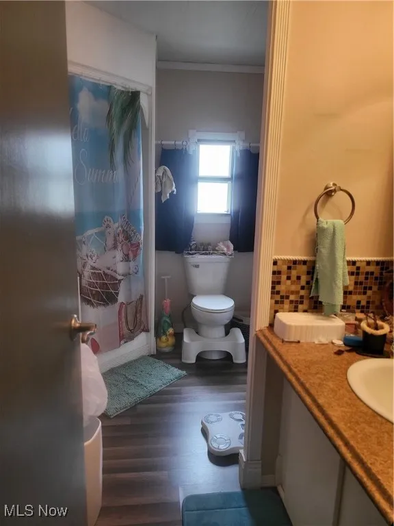 Bathroom with curtained shower, toilet, crown molding, wood finished floors, and decorative backsplash