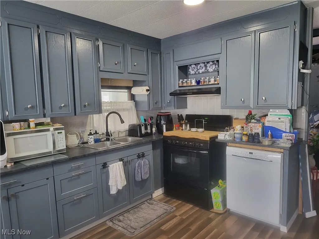 Kitchen featuring white appliances, dark wood-type flooring, open shelves, under cabinet range hood, and a sink