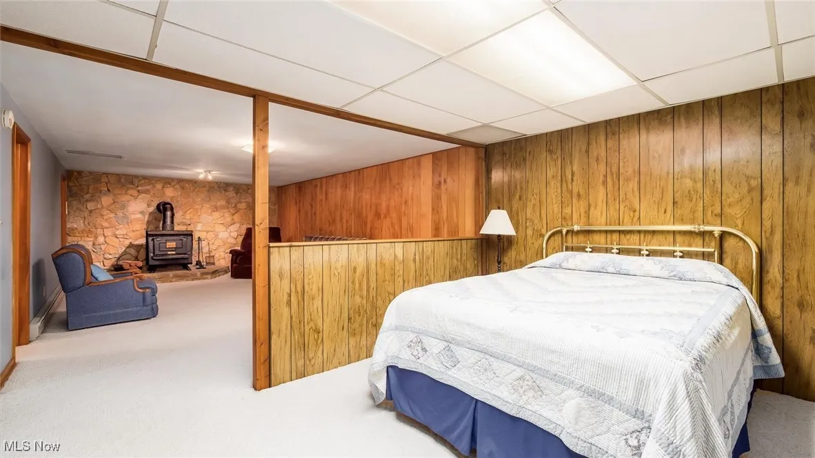 Bedroom with wood walls, a wood stove, carpet flooring, and a drop ceiling