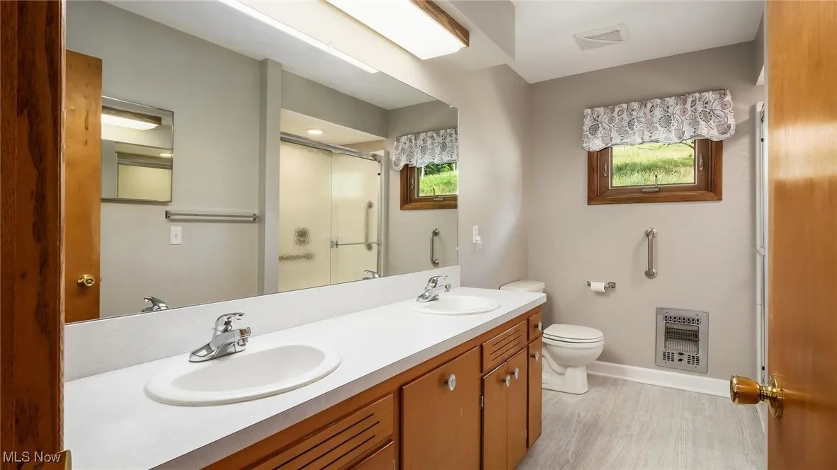 Full bathroom with toilet, a stall shower, a sink, and heating unit