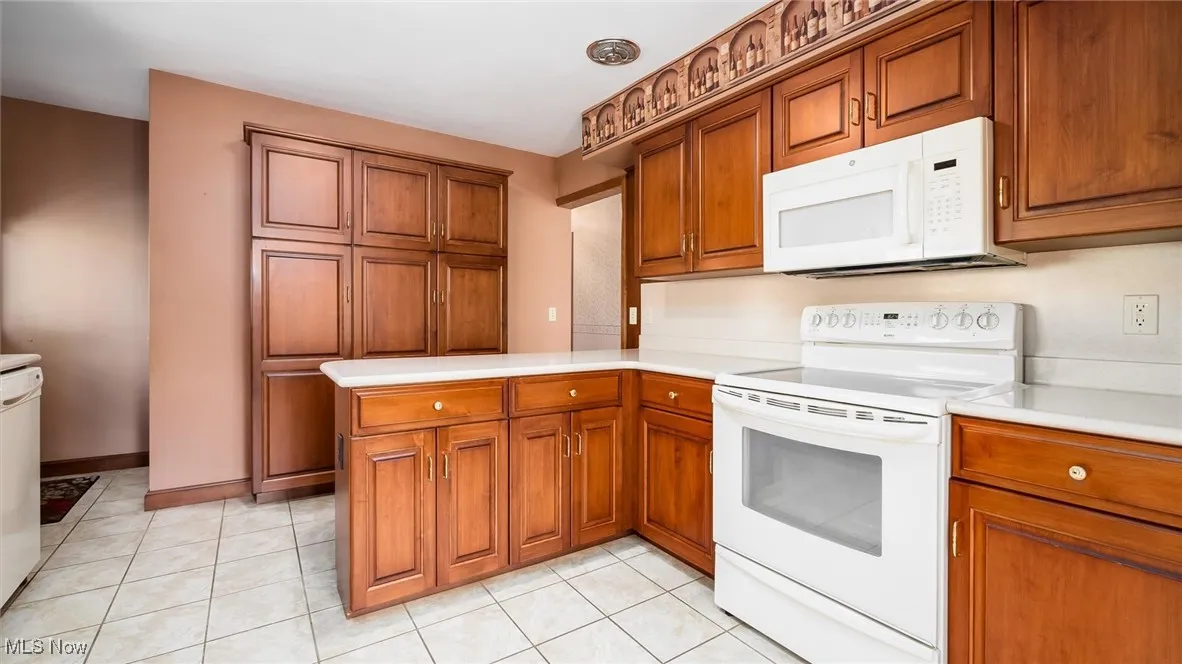 Kitchen with light tile patterned floors, white appliances, brown cabinetry, a peninsula, and light countertops