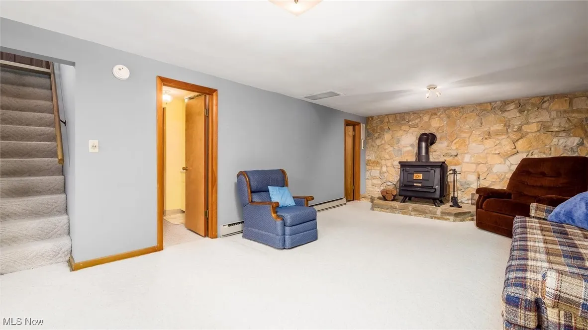 Living area with a wood stove, carpet, stairway, baseboard heating, and baseboards