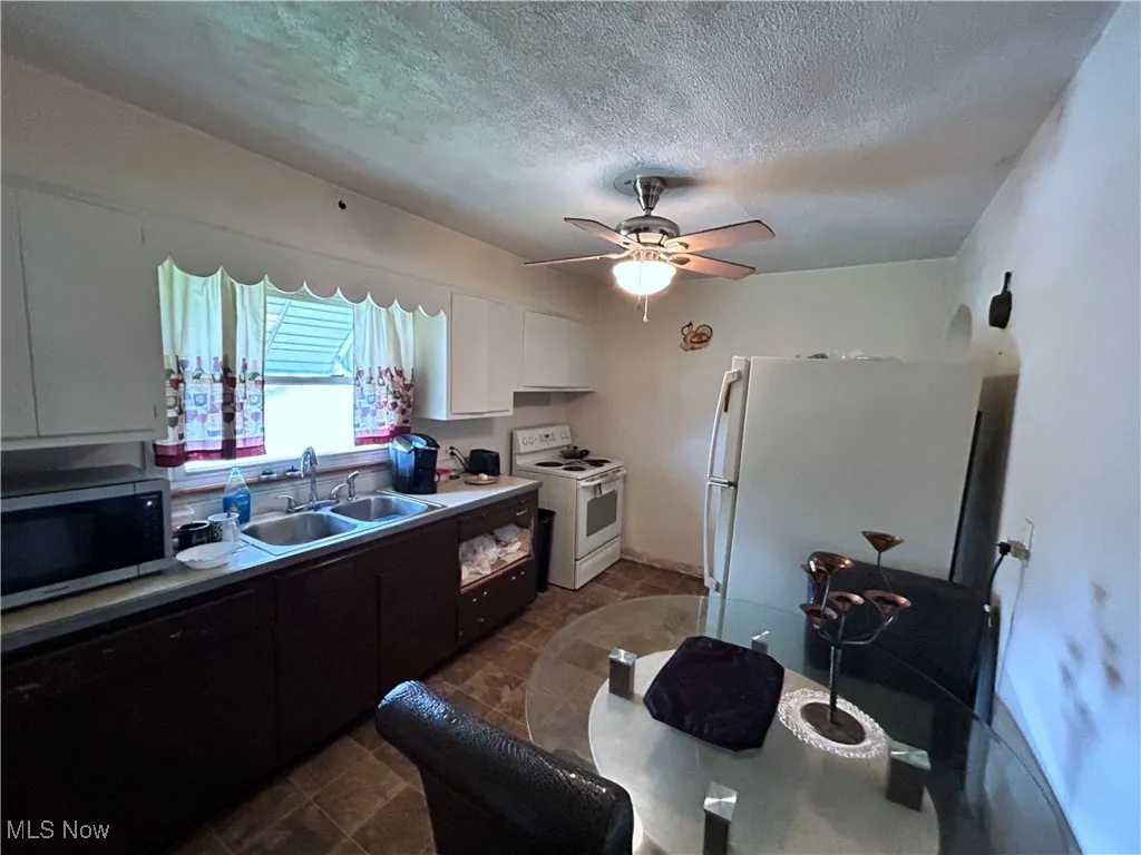 Kitchen with a textured ceiling, white cabinetry, a sink, and white appliances