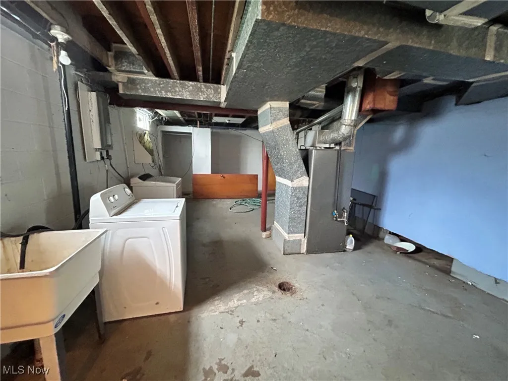Unfinished basement with washer / dryer, a sink, heating unit, and concrete block wall