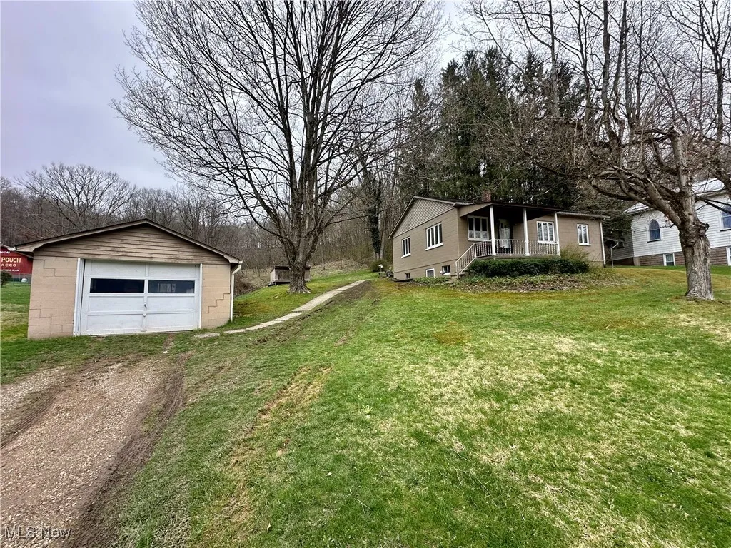 View of yard featuring a porch, an outbuilding, a detached garage, and dirt driveway