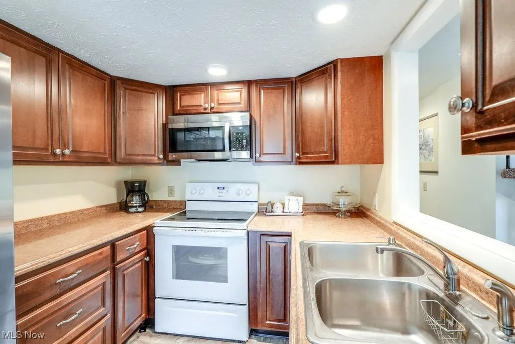 Kitchen with stainless steel microwave, recessed lighting, light countertops, a sink, and white range with electric cooktop