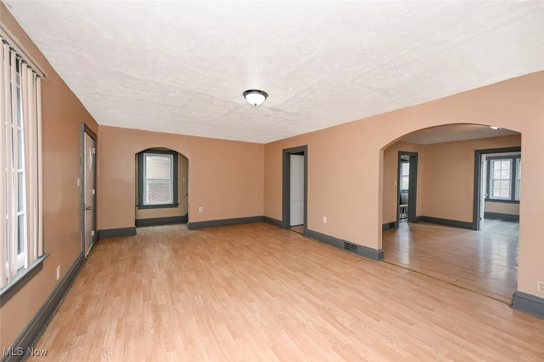 Spare room featuring arched walkways, light wood-type flooring, a textured ceiling, visible vents, and baseboards