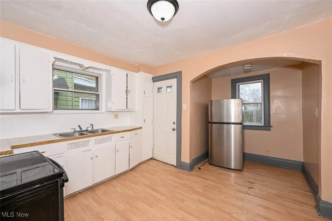 Kitchen featuring white cabinets, arched walkways, a sink, and freestanding refrigerator
