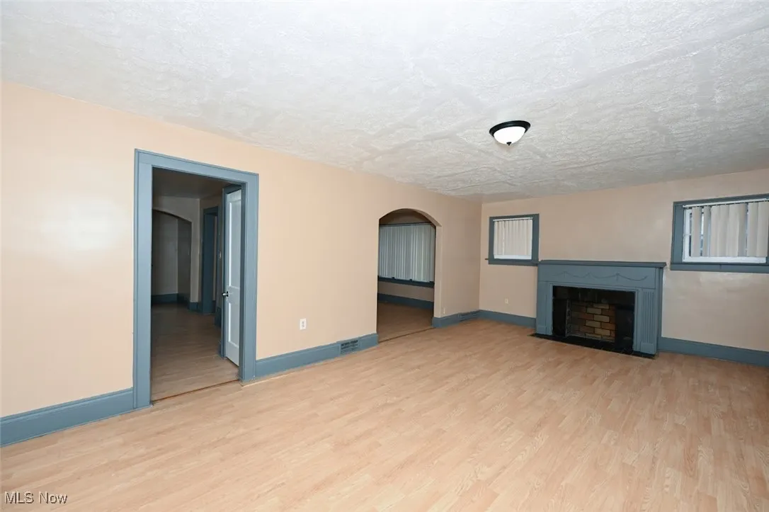 Unfurnished living room featuring baseboards, a fireplace with flush hearth, light wood-type flooring, and a textured ceiling