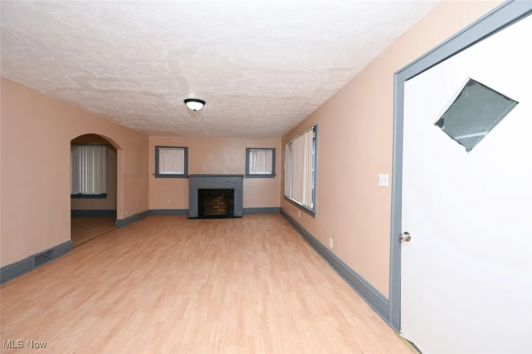 Unfurnished living room featuring visible vents, arched walkways, a textured ceiling, a fireplace, and light wood finished floors