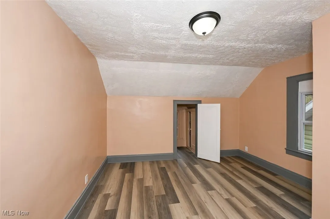 Additional living space with a textured ceiling, wood finished floors, baseboards, and vaulted ceiling