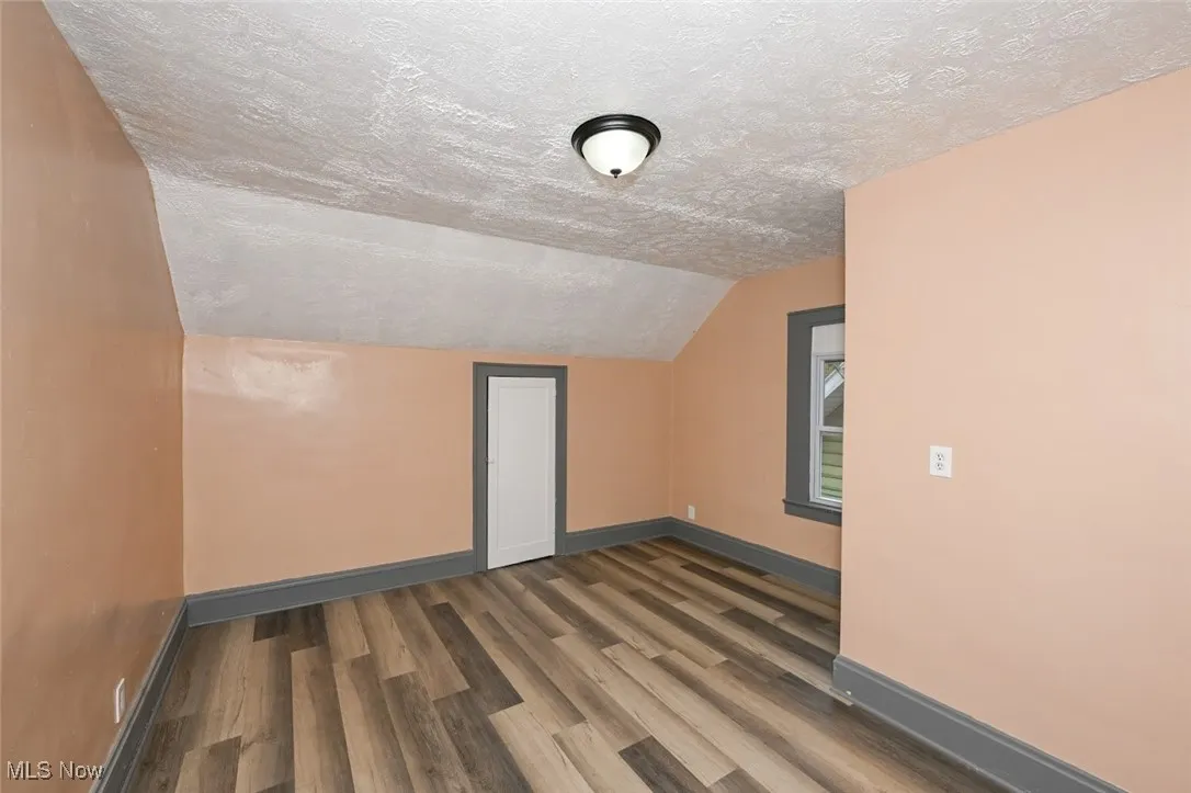 Bonus room with lofted ceiling, a textured ceiling, baseboards, and wood finished floors