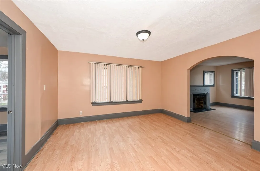 Unfurnished living room with light wood-style floors, a fireplace with flush hearth, arched walkways, a textured ceiling, and baseboards
