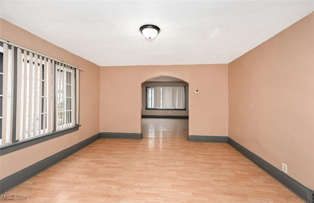 Empty room with arched walkways, light wood-style flooring, and baseboards