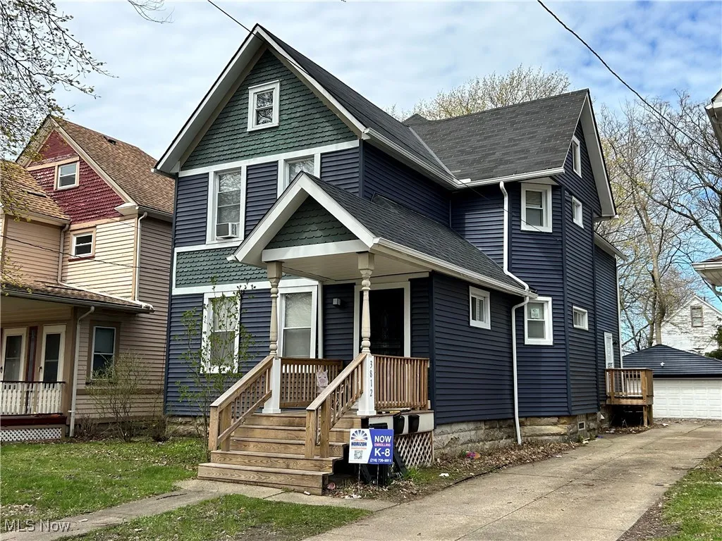 View of front of home with an outbuilding, a detached garage, a porch, and roof with shingles