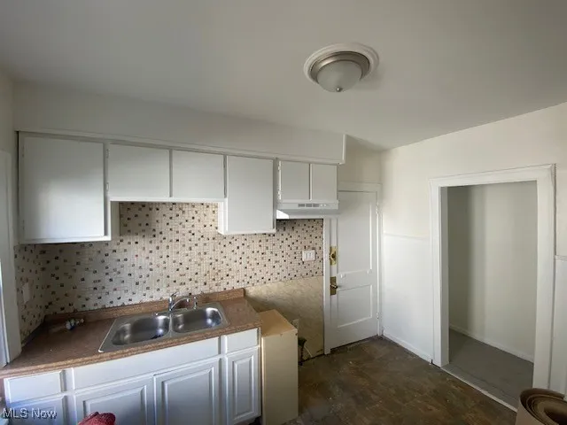 Kitchen with tasteful backsplash, dark wood-style floors, white cabinets, and under cabinet range hood