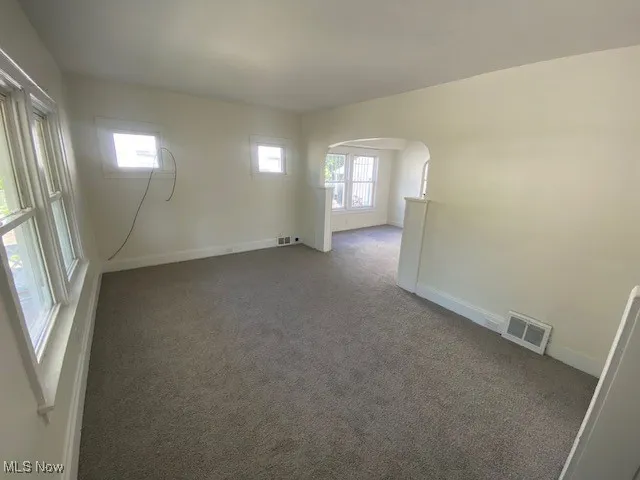 Carpeted empty room featuring arched walkways and baseboards