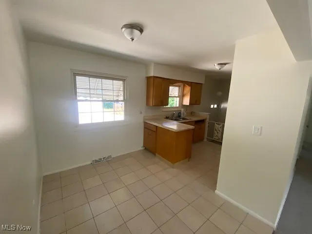 Kitchen featuring brown cabinetry, light countertops, a peninsula, and light tile patterned floors
